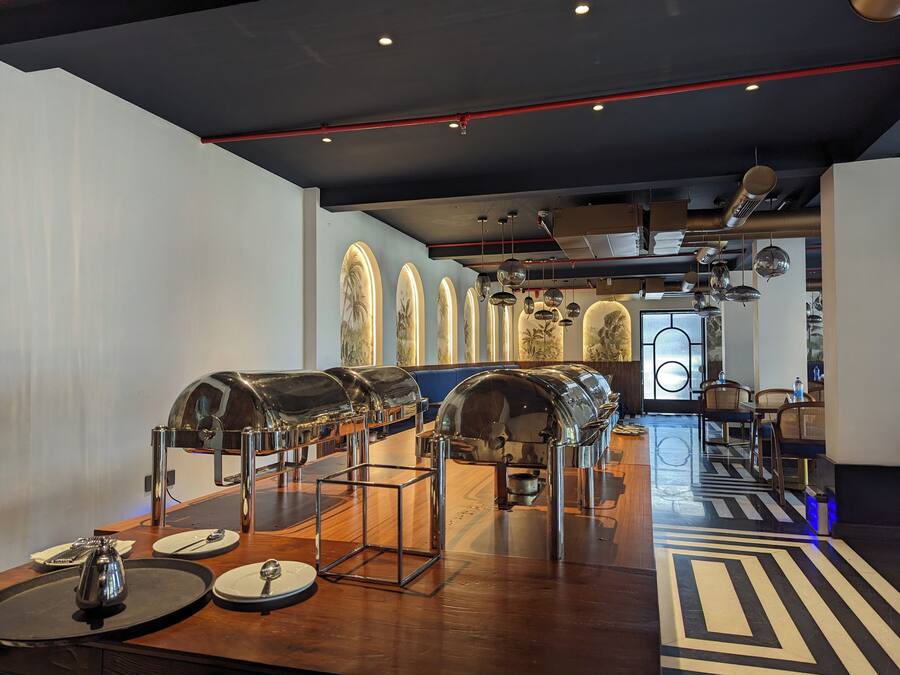 A modern restaurant interior with a long counter, metal serving stations, and a patterned floor.