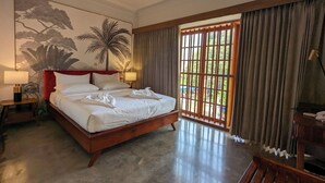 A spacious bedroom with a large bed, a ceiling fan, a nightstand with a lamp, a wooden headboard, a large window with curtains, and a wall mural.