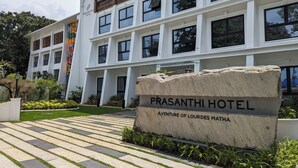 A modern hotel building with a sign reading "Prasanthi Hotel" and "A Venture of Lourdes Matha".