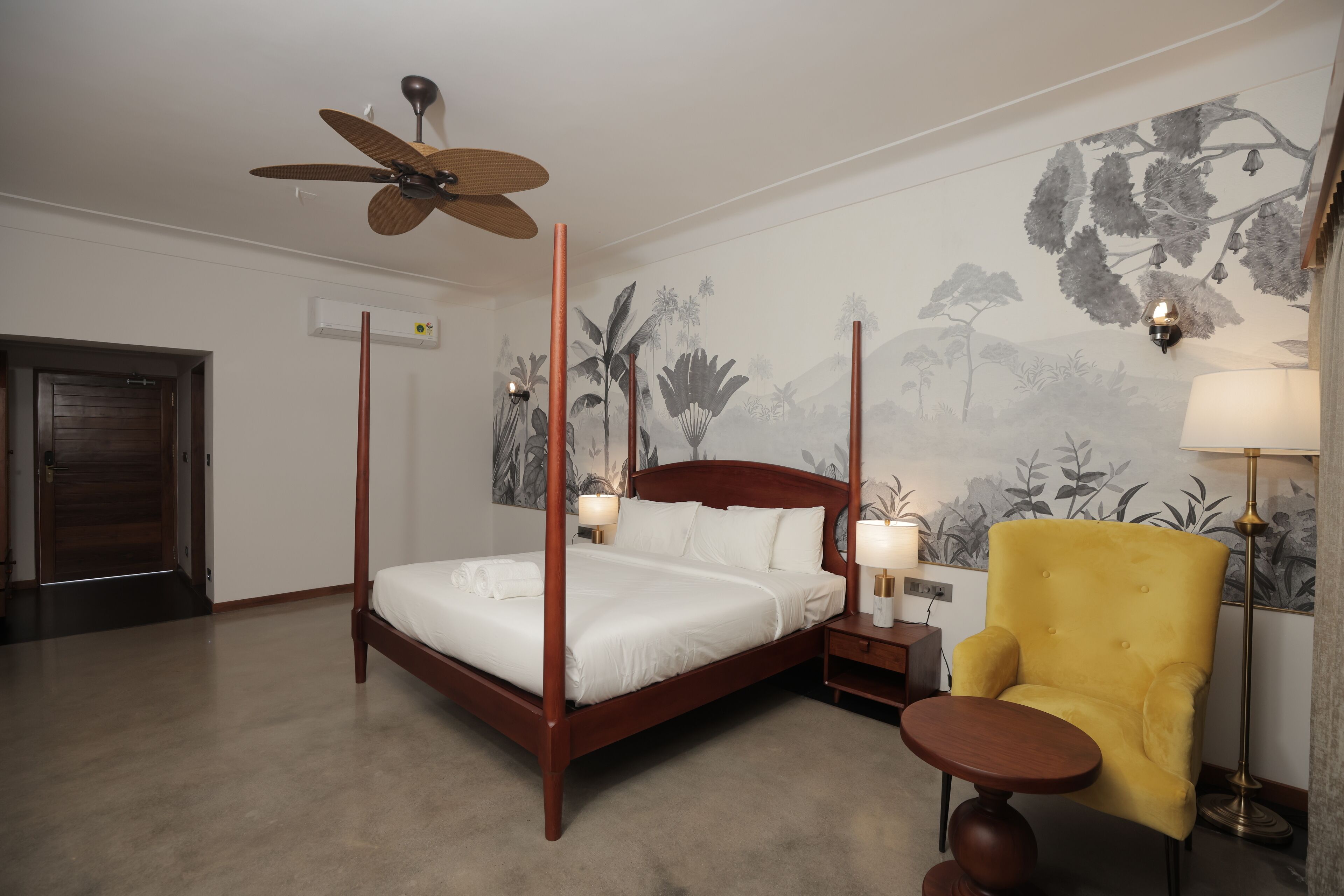 A four-poster bed with a ceiling fan, a yellow armchair, and a nightstand with lamps.