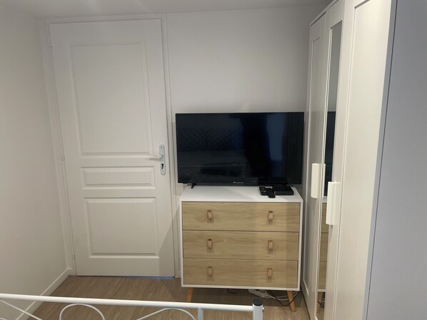 A room with a white wardrobe, a TV on a white stand, and a wooden dresser with drawers.