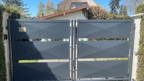 A metal gate with a plaque reading "21 bis" and a house with a thatched roof in the background.