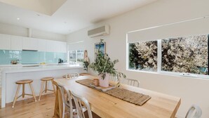Cozinha moderna com armários brancos, uma ilha central e área de refeições com mesa e banquetas de madeira.