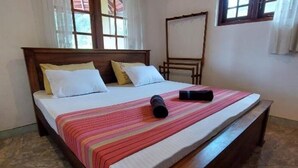Una cama con cabecera de madera, almohadas blancas y amarillas, colcha a rayas y un objeto negro sobre la cama.