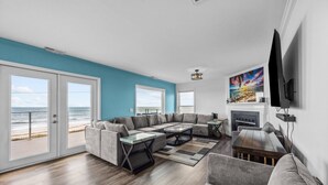 A living room with a sectional sofa, a coffee table, and a fireplace. There are large windows with a view of the beach. - Summer Winds #191 - Ocean Views, Hot Tub & Steps to the Beach! Dog Friendly! (North Topsail Beach)