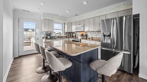 A modern kitchen with a large island, stainless steel appliances, and a view to the outside. - Summer Winds #191 - Ocean Views, Hot Tub & Steps to the Beach! Dog Friendly! (North Topsail Beach)