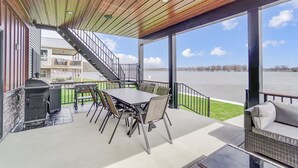Eine überdachte Terrasse im Freien mit Tisch, Stühlen, einem Grill und Blick auf ein Gewässer.