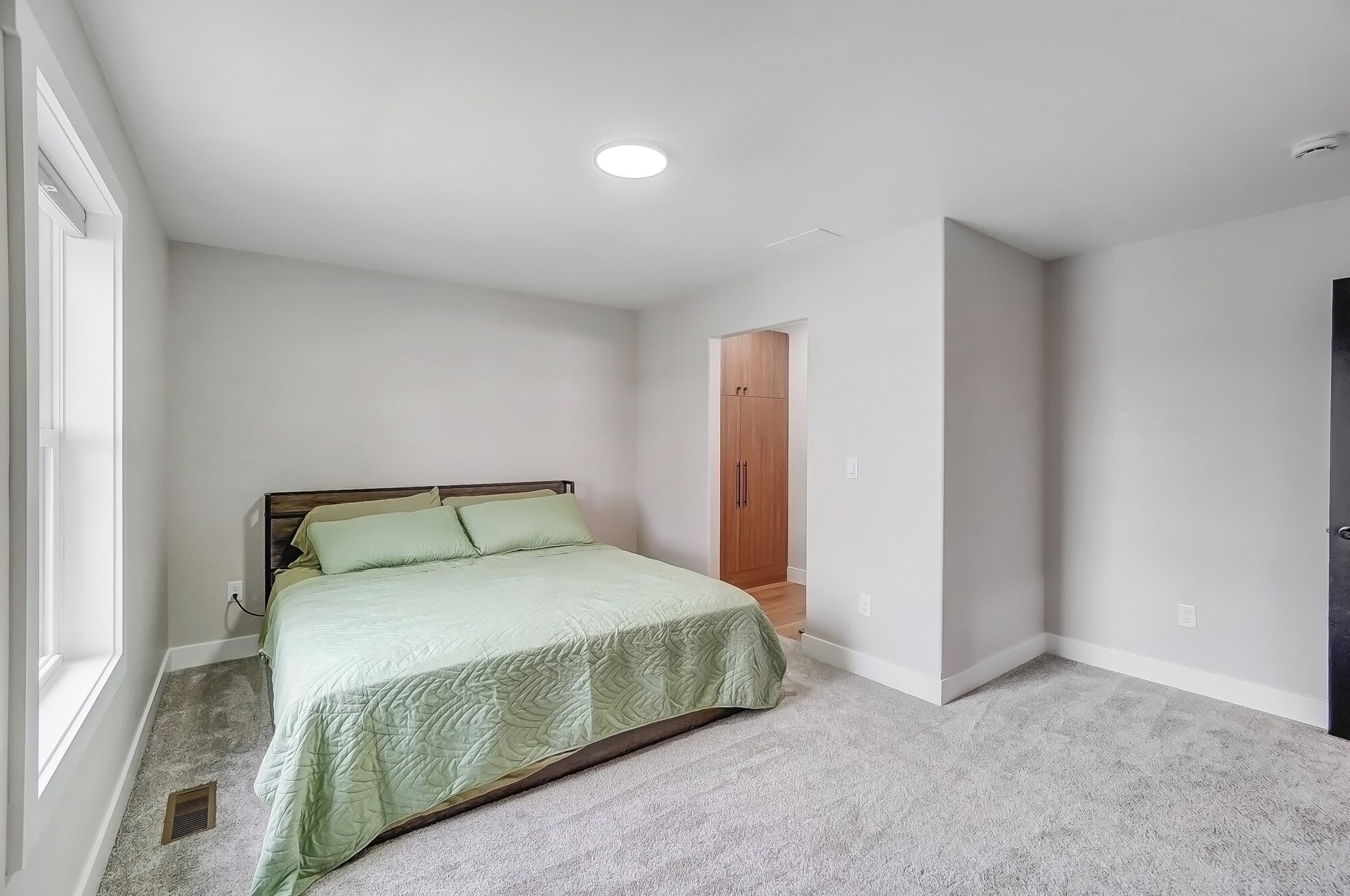 A bedroom with a bed, a wooden wardrobe, and a door.
