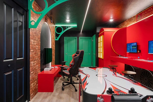 A modern gaming room with a large desk, gaming chair, and multiple monitors.