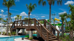 Uma área de piscina com uma ponte de madeira, palmeiras e um toboágua.