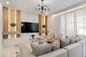 A modern living room with a sofa, coffee table, TV, and decorative plants.