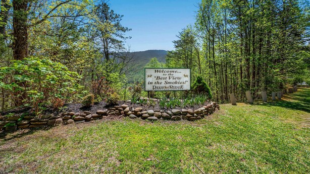 A welcome sign at the entrance of Deer Ridge with a view of a forested area and hills in the background. - Luxe Condo - Mountain Views - Pool Hot Tub Sauna (Gatlinburg)