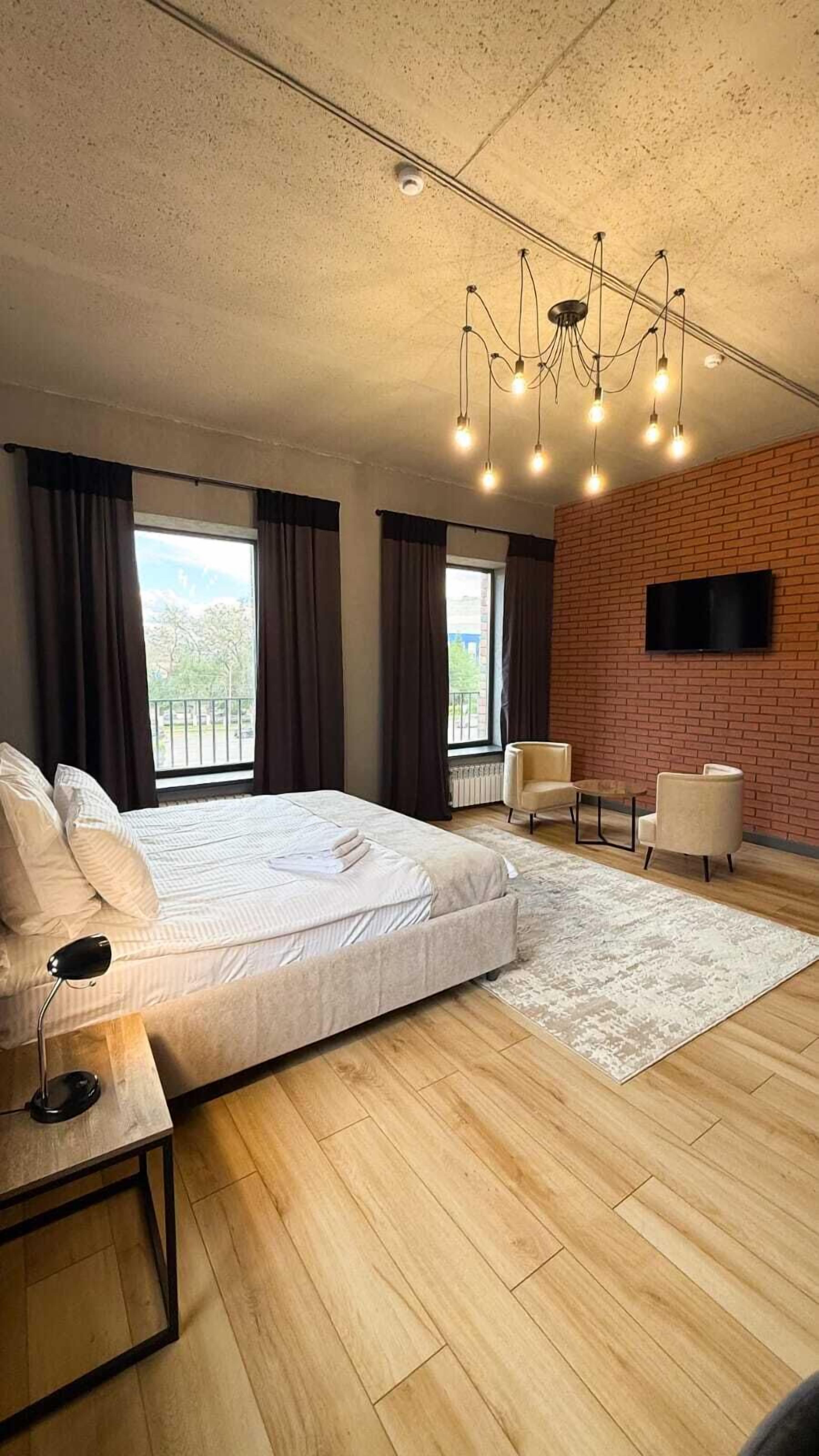 A modern bedroom with a large bed, a desk, a chair, and a TV mounted on a brick wall.