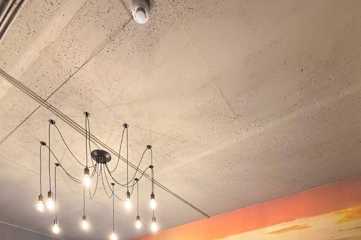 A bedroom with a large bed, a nightstand, a wardrobe, a chandelier, and a mural of a sunset.