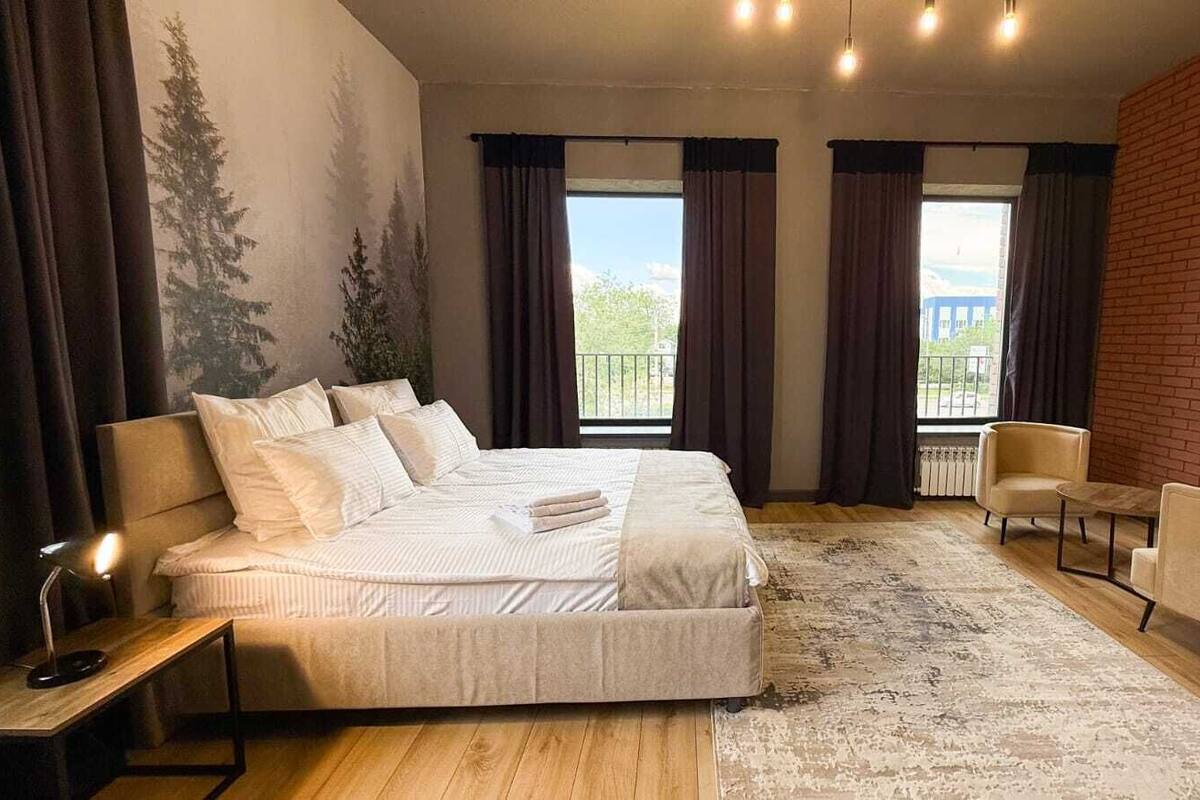 A bedroom with a large bed, a desk, a chair, and a view of the outdoors.