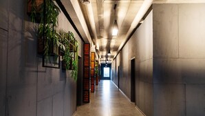 A long, narrow hallway with a tiled floor, concrete walls, and hanging plants. - Avenue Hotel (Uralsk)