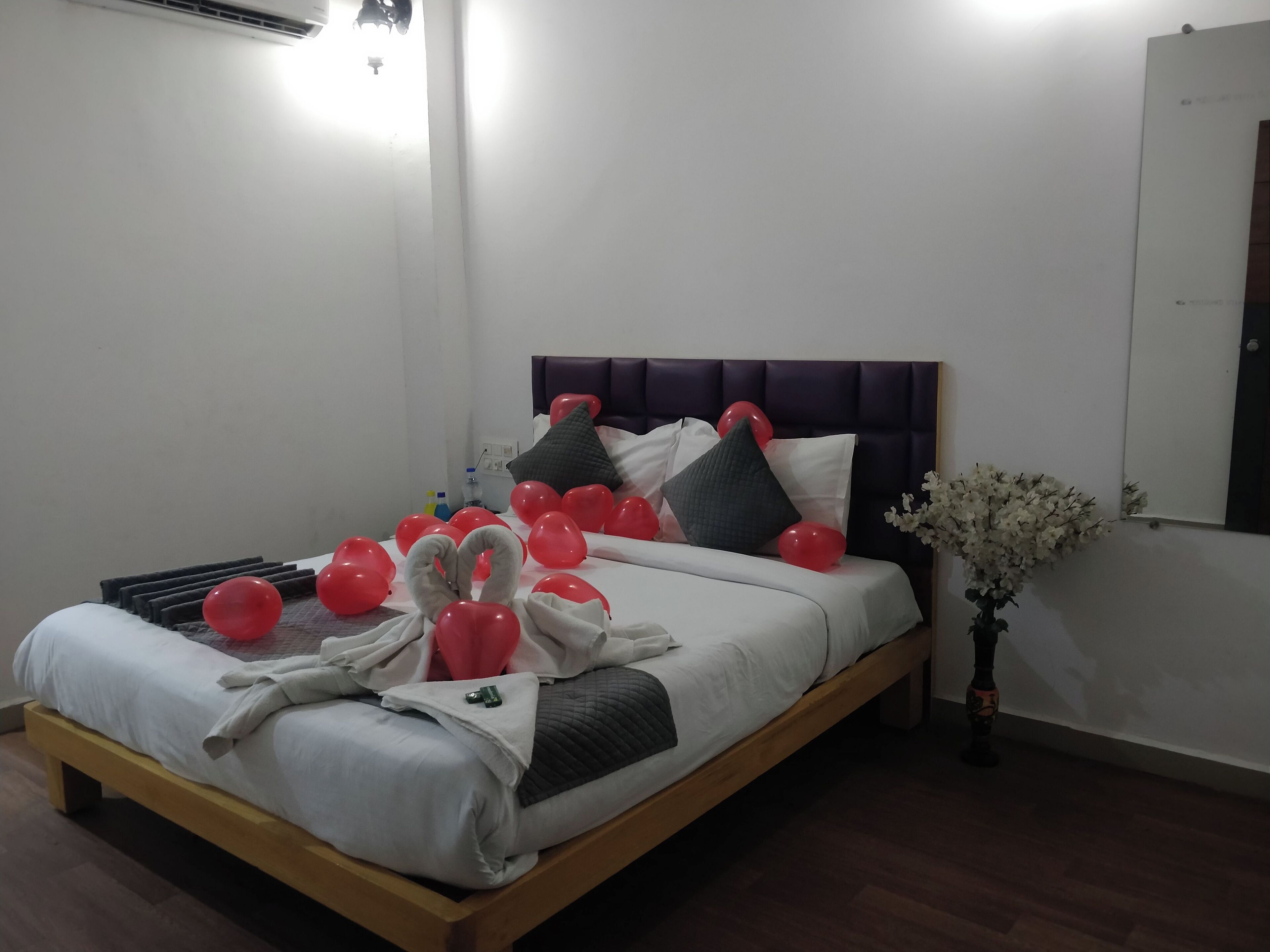 A neatly made bed with a wooden frame, white bedding, and red heart-shaped balloons.