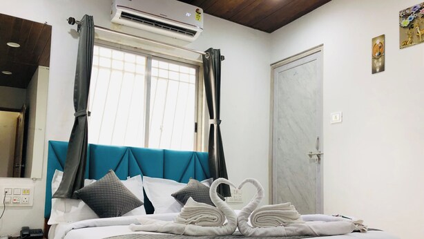 A neatly made bed with a teal headboard, a wall-mounted air conditioner, and a door with a marble finish. - Hotel Silk (Surat)