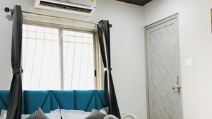 A hotel room with a bed, a ceiling fan, an air conditioning unit, a window with curtains, and a door. - Hotel Silk (Surat)
