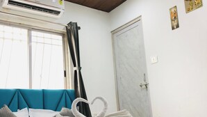 A hotel room with a bed, a ceiling fan, an air conditioning unit, a window with curtains, and a door. - Hotel Silk (Surat)