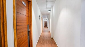 A hallway with wooden doors, white walls, and a tiled ceiling. - Hotel Silk (Surat)