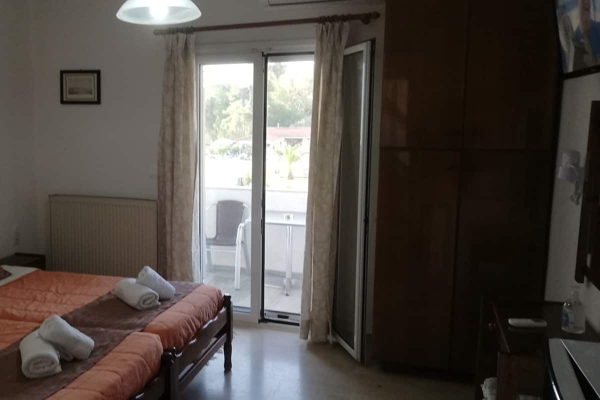 A hotel room with a bed, a radiator, a window with curtains, and a view of the outside.