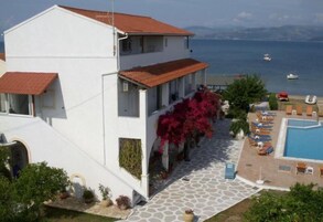Un edificio blanco con techo de tejas rojas que da a una zona de piscina con sillones de descanso y vistas al mar.