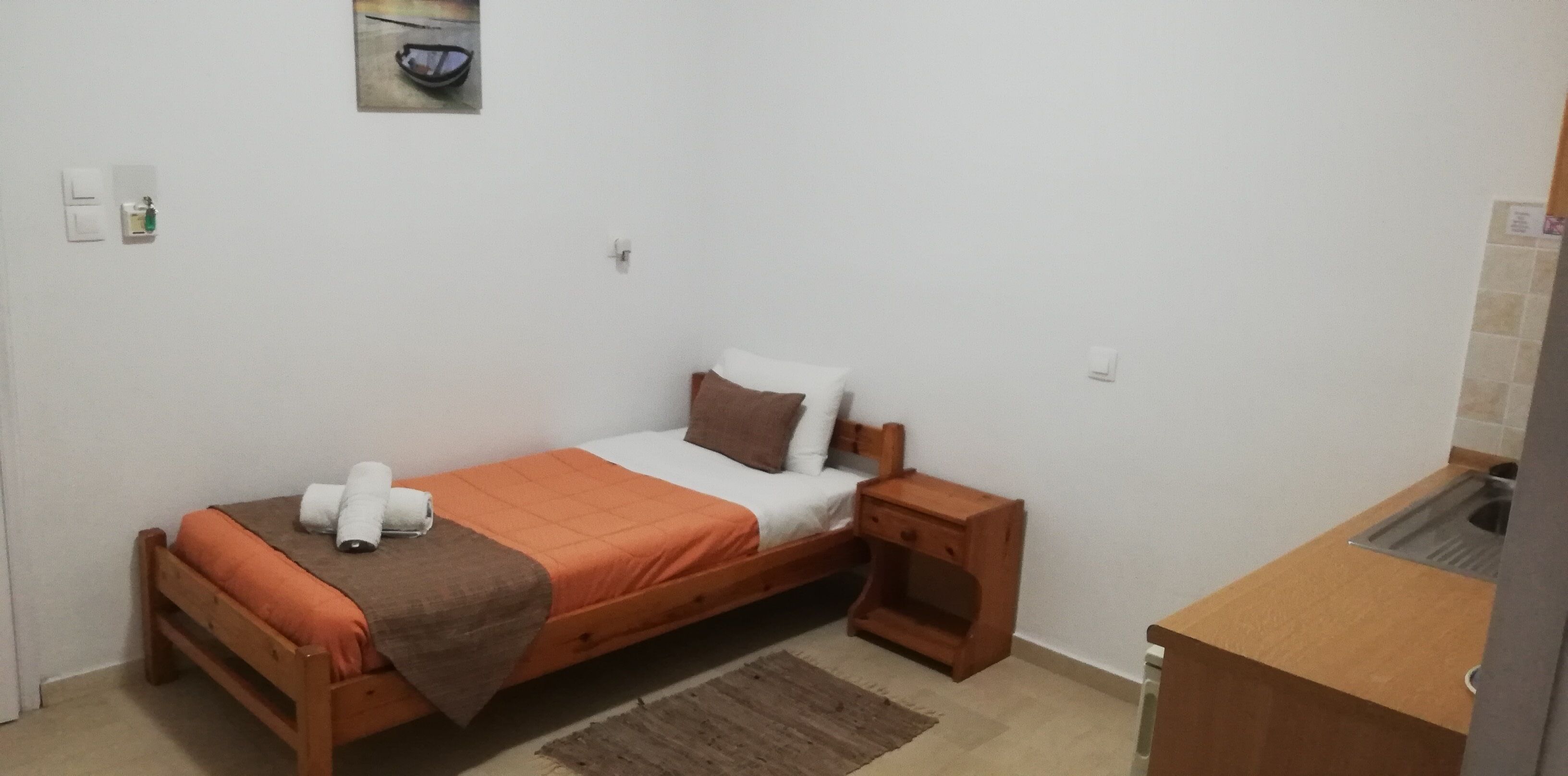 A small, single-bed room with a wooden bed frame, a brown blanket, and a wooden nightstand with a drawer.