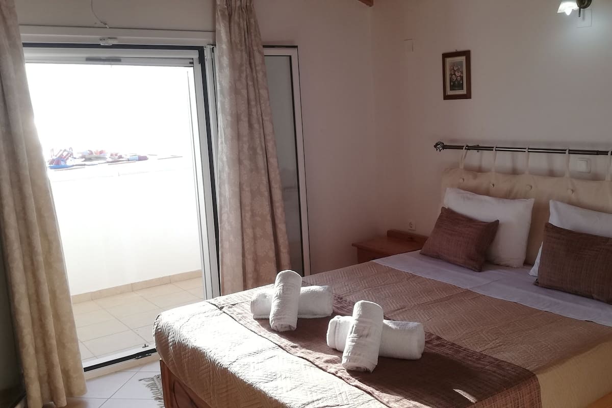 A hotel room with a bed, a window with curtains, a bedside table, and a view of the outside.