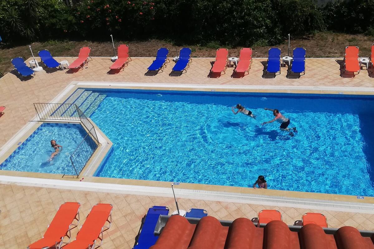 A rectangular swimming pool with multiple lanes, surrounded by sun loungers in red and blue.