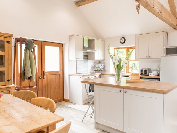 Une cuisine avec des meubles blancs, une table en bois et une fenêtre laissant entrer la lumière naturelle.
