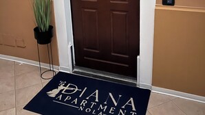 A brown door with a white frame, a doormat with "Diana Apartment Nola" text, and a sign above the door.