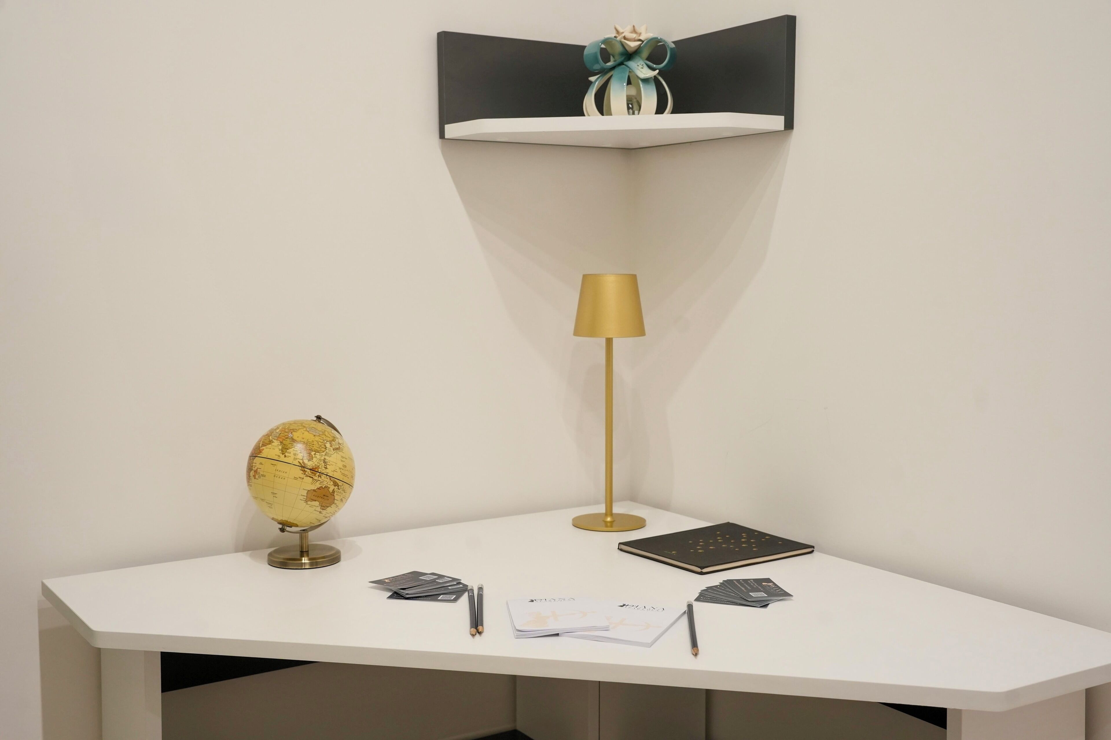 Ein weißer Schreibtisch mit einem Globus, einer Lampe und einem schwarzen Notizbuch.
