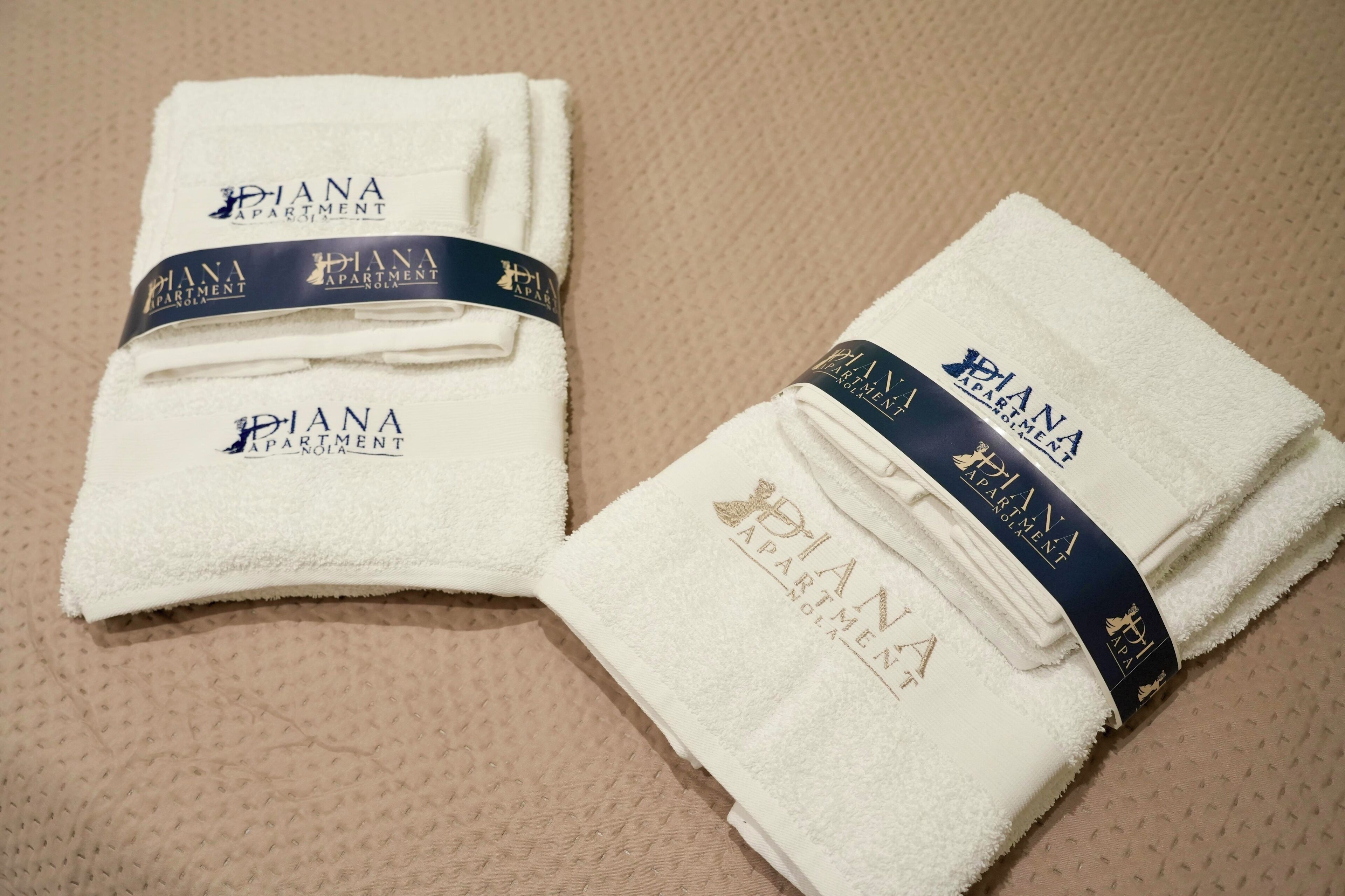 Two folded white towels with 'Diana Apartment' branding and a dark blue ribbon.