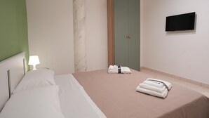 A hotel room with a bed, a nightstand with a lamp, a wardrobe, and a flat-screen TV on the wall.