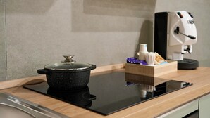 A kitchen with a black induction cooktop, a pot on it, a coffee machine, and a box with snacks.
