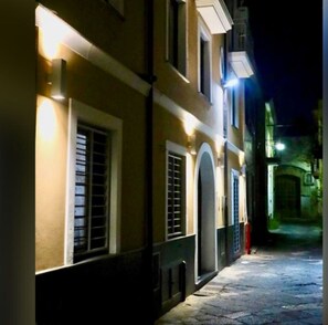 Une rue étroite, bordée de bâtiments des deux côtés, éclairée par des lampadaires.