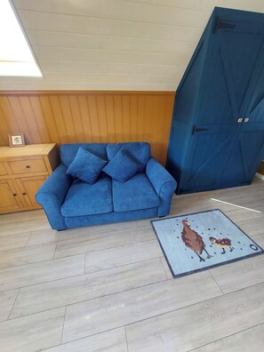 Una habitación con un sofá azul, un armario de madera, una puerta azul y un suelo con alfombra estampada.