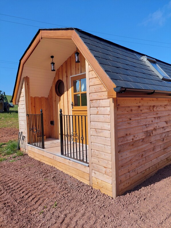 Una cabaña de madera con techo inclinado, puerta principal con paneles de vidrio y un pequeño porche con barandilla.