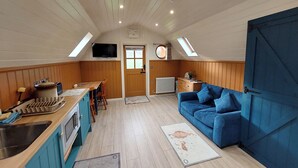Eine kleine Küche mit Spüle, Herd und Holzschränken. Im Wohnbereich befindet sich ein blaues Sofa und ein kleiner Tisch mit Stühlen.