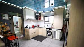 A modern kitchen with a washing machine, a coffee machine, and a dining area with a red chair.