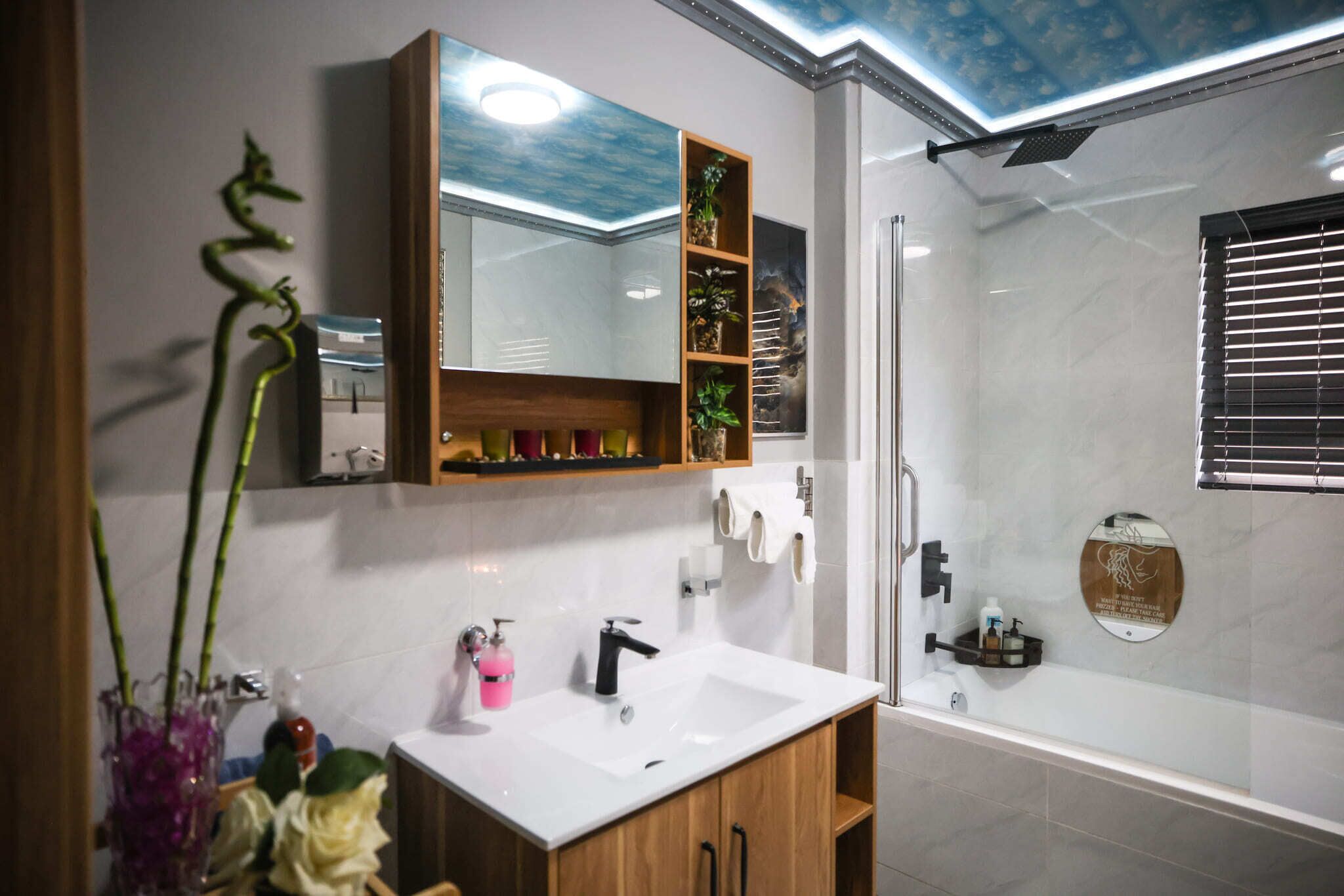 A bathroom with a white sink, wooden cabinet, mirror, and a shower area.