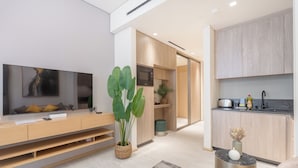 A modern living room with a flat-screen TV, wooden furniture, a large plant, and a kitchen area with a sink and countertop. - Czechin - Modern Studio JVC  (Dubai)