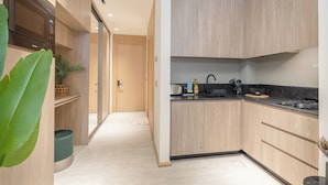 A modern kitchen with wooden cabinets, a black countertop, and a sink. There is a microwave on the left and a plant on the right. - Czechin - Modern Studio JVC  (Dubai)