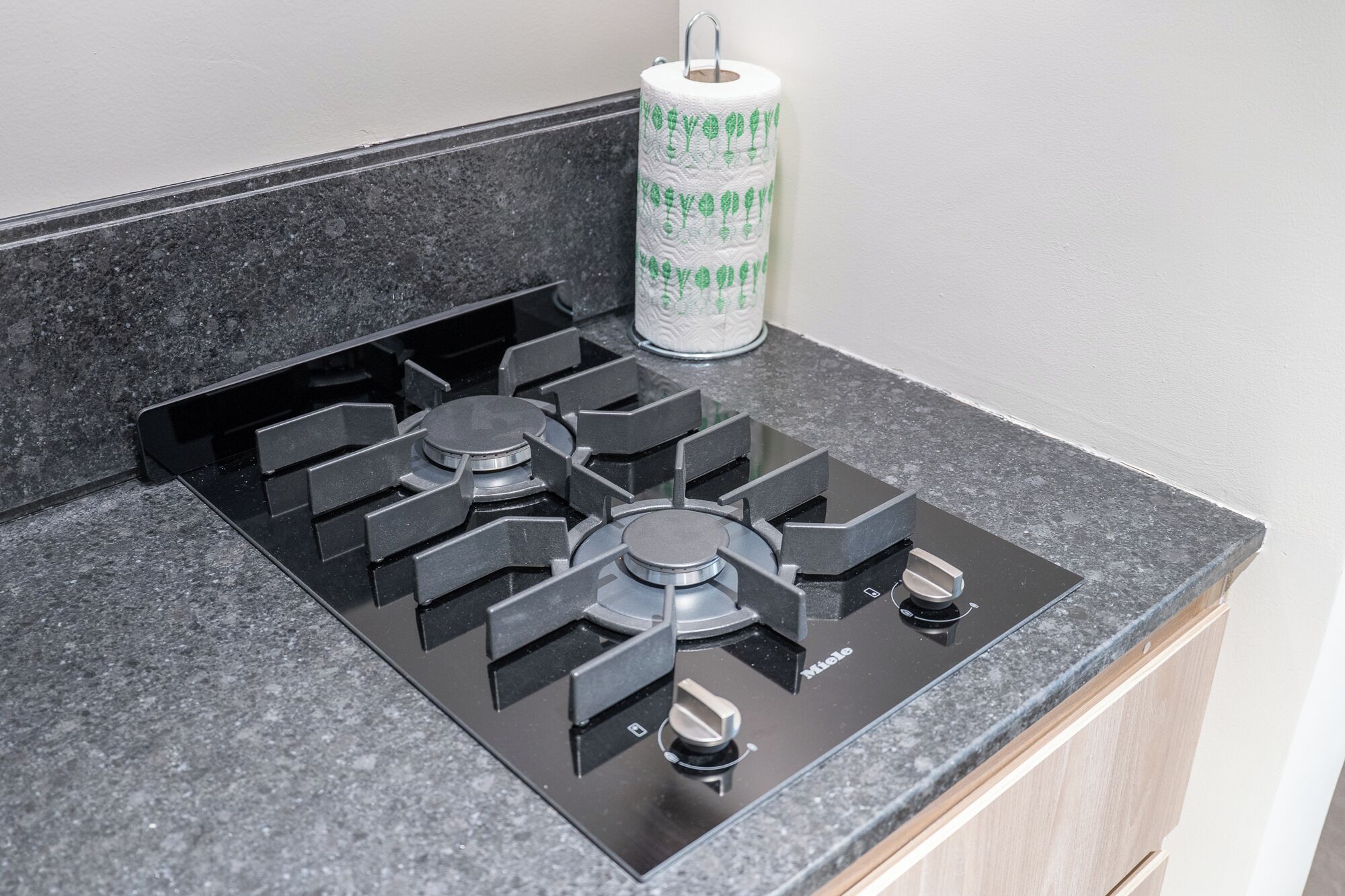 A kitchen with a black gas stove, a roll of paper towels, and a granite countertop.