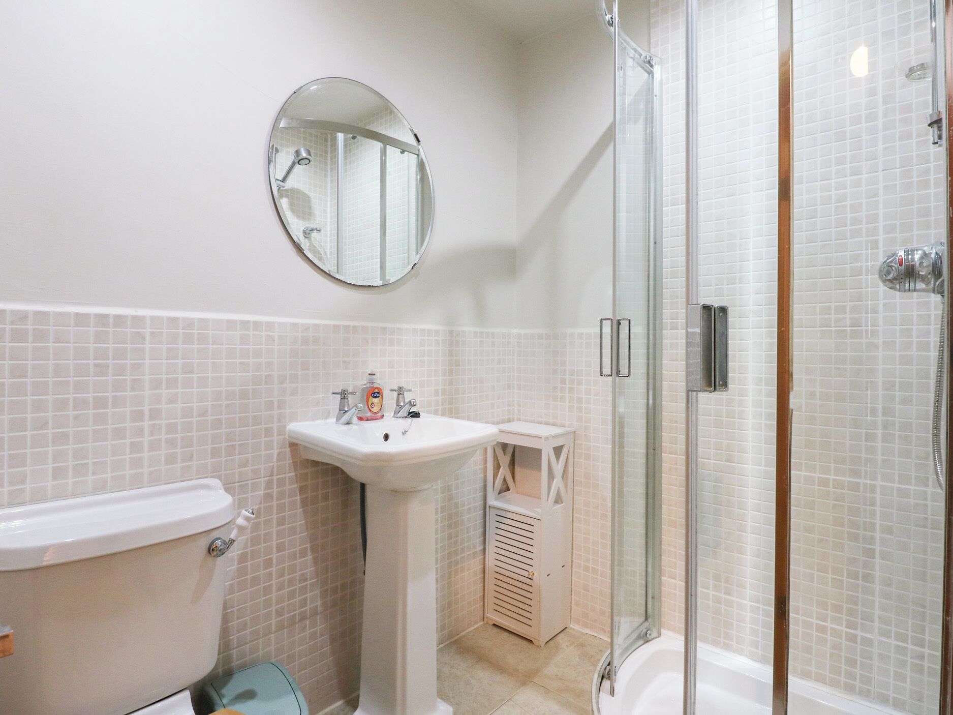 A bathroom with a toilet, pedestal sink, and a glass-enclosed shower area.