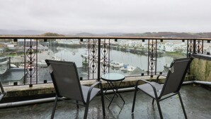 Un balcone con due sedie e un tavolino, affacciato su una marina con barche ed edifici.
