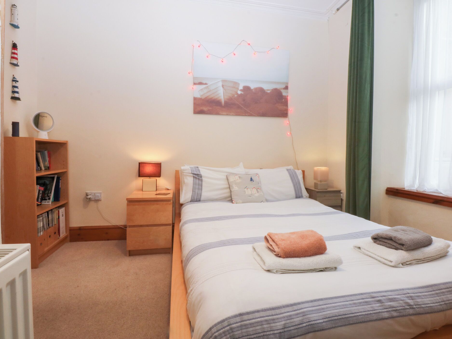 Een slaapkamer met een bed, nachtlampjes, een boekenkast en een aan de muur hangend schilderij.