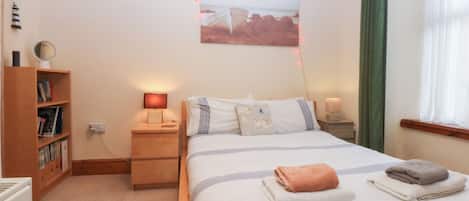 A bedroom with a bed, bedside lamps, a bookshelf, and a wall-mounted picture.
