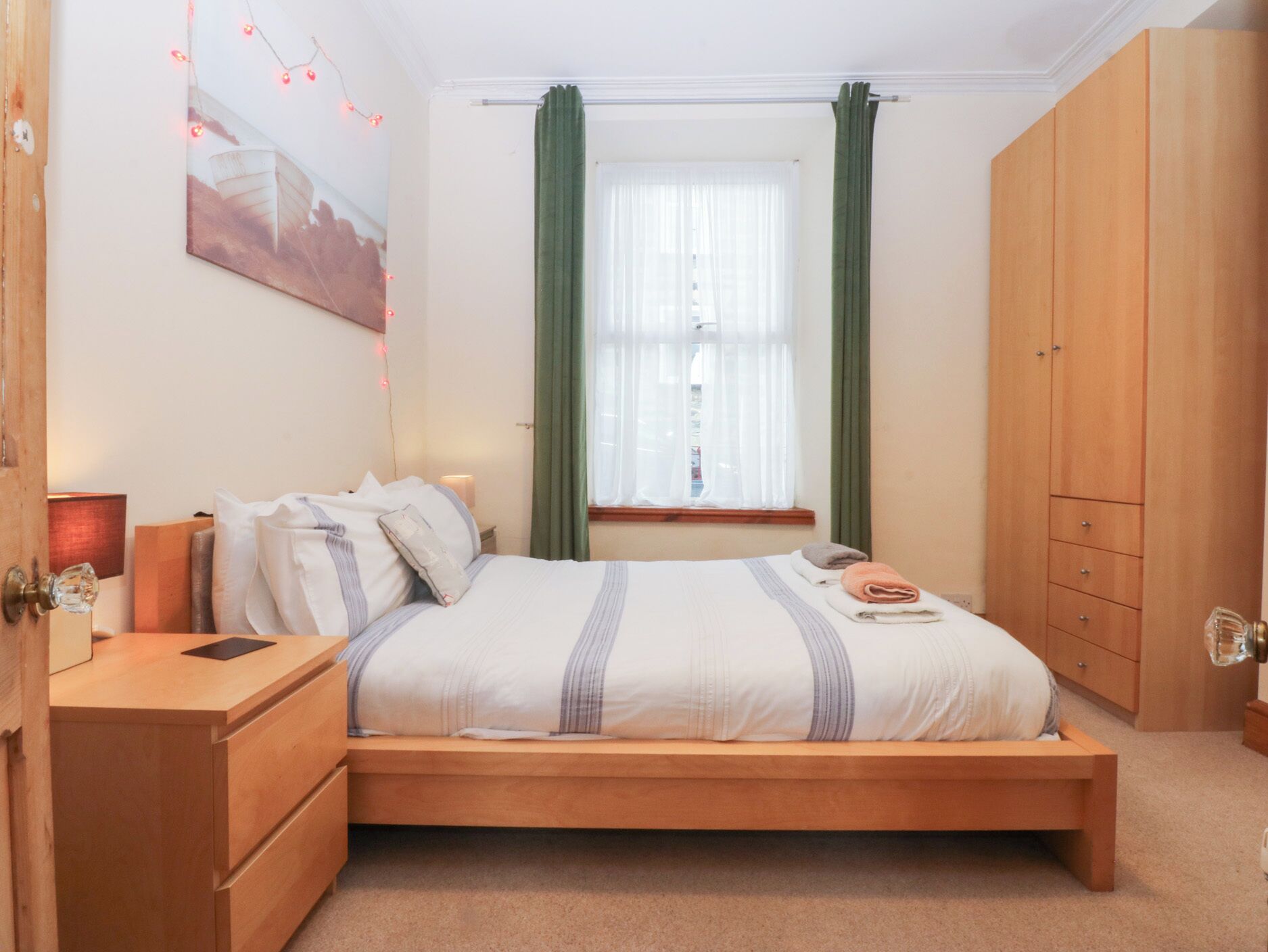 A bedroom with a wooden bed, a nightstand, a wardrobe, and a window with curtains.